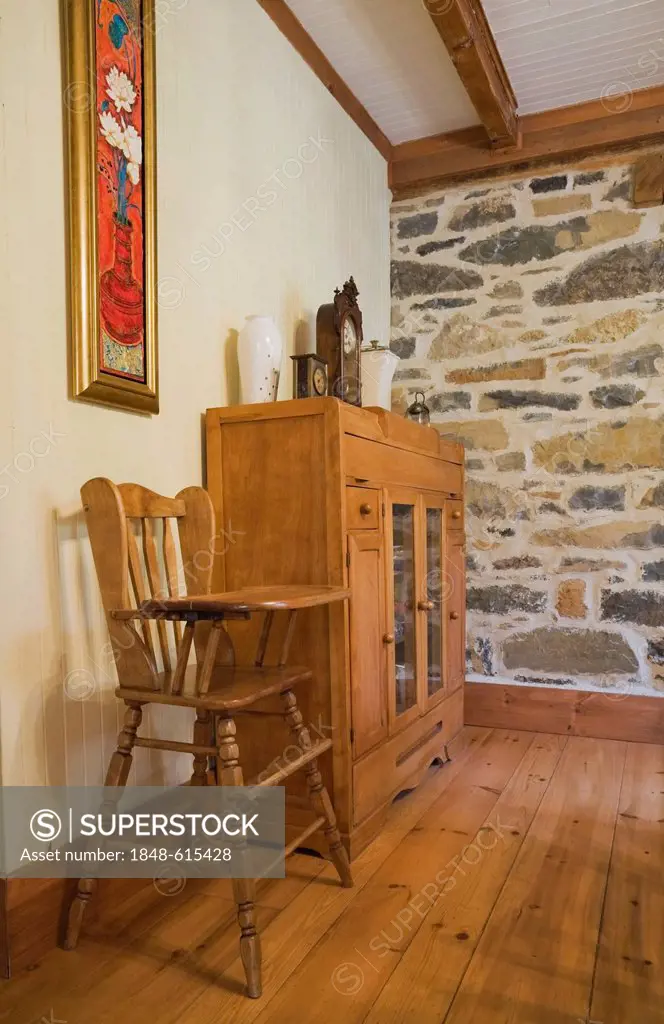 High chair and small dresser in the dining room of an old Canadiana cottage-style residential fieldstone home, circa 1832, Laurentians, Quebec, Canada...
