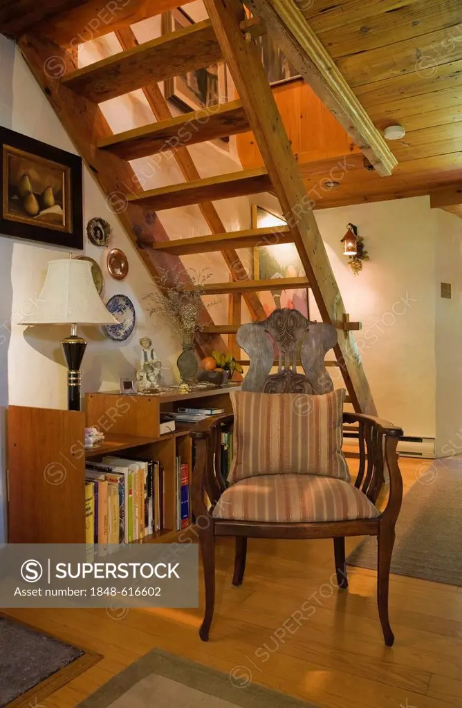 Chair and bookcase beneath the stairs in an old Canadiana cottage-style residential fieldstone home, circa 1740, Quebec, Canada. This image is propert...