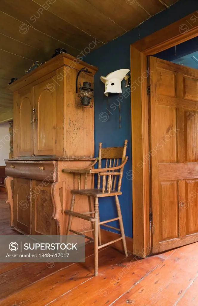 Antique pinewood armoire and high chair in the dining room of an old Canadiana cottage-style residential log home, circa 1840, Quebec, Canada. This im...