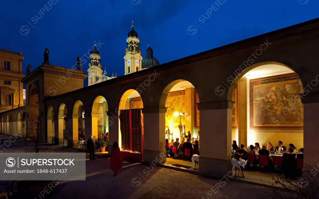 People sitting underneath the arcades of the Luigi Tambosi Cafe on Odeonsplatz square, Theatinerkirche church at the back, Munich, Bavaria, Germany, E...