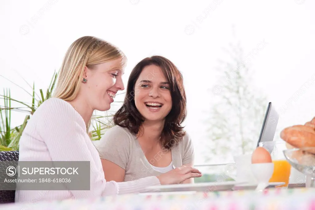 Two young women using a laptop while having breakfast on a terrace