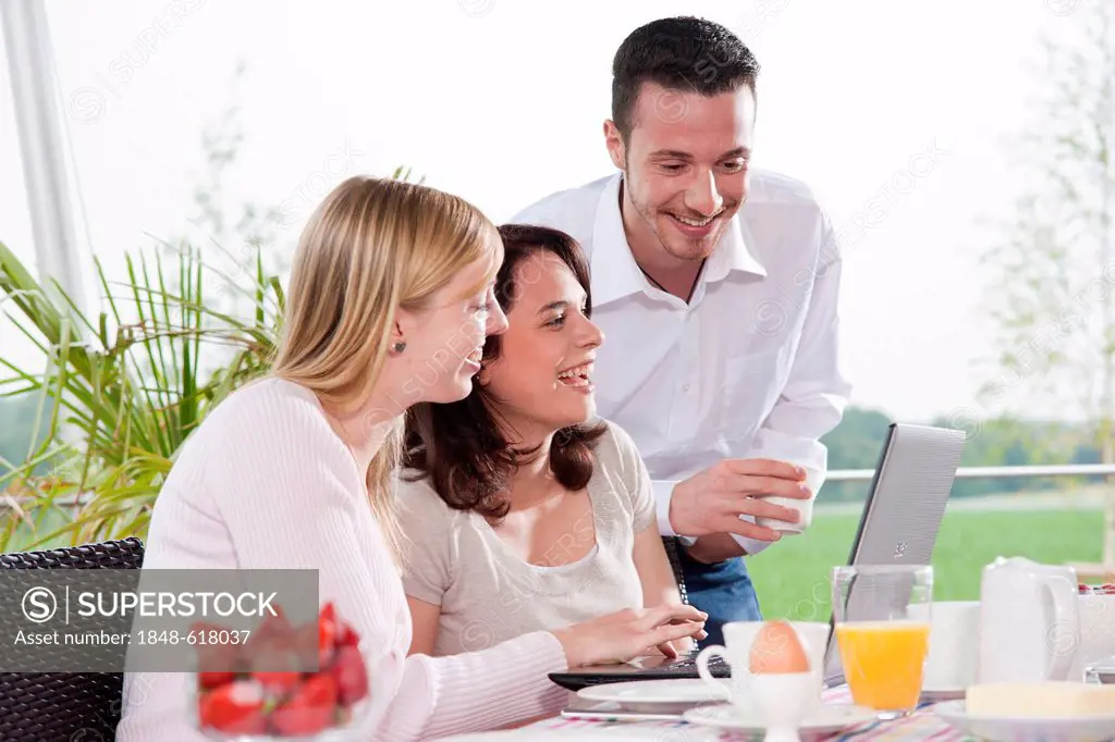 Young people using a laptop while having breakfast on a terrace