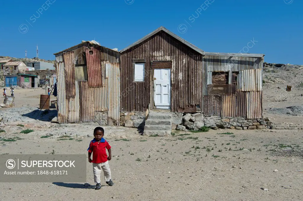 Child standing in front of an old corrugated iron house, outskirts of Luederitz, Namibia, Africa