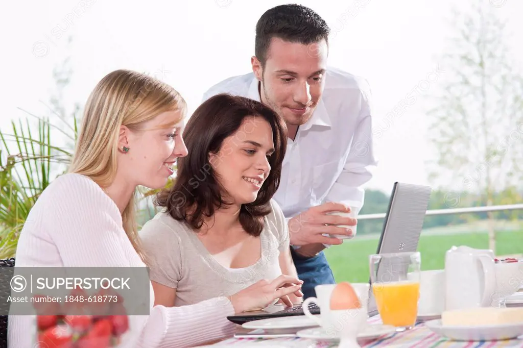Young people using a laptop while having breakfast on a terrace
