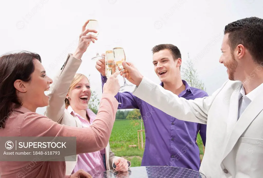 A group of young people chinking glasses, celebrating on a terrace