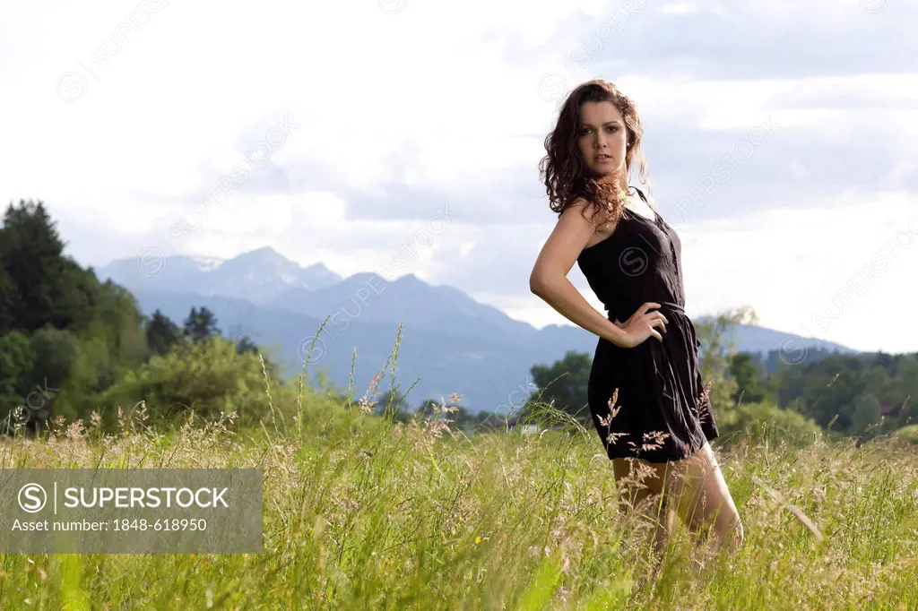 Young woman posing in a short black dress in the long grass