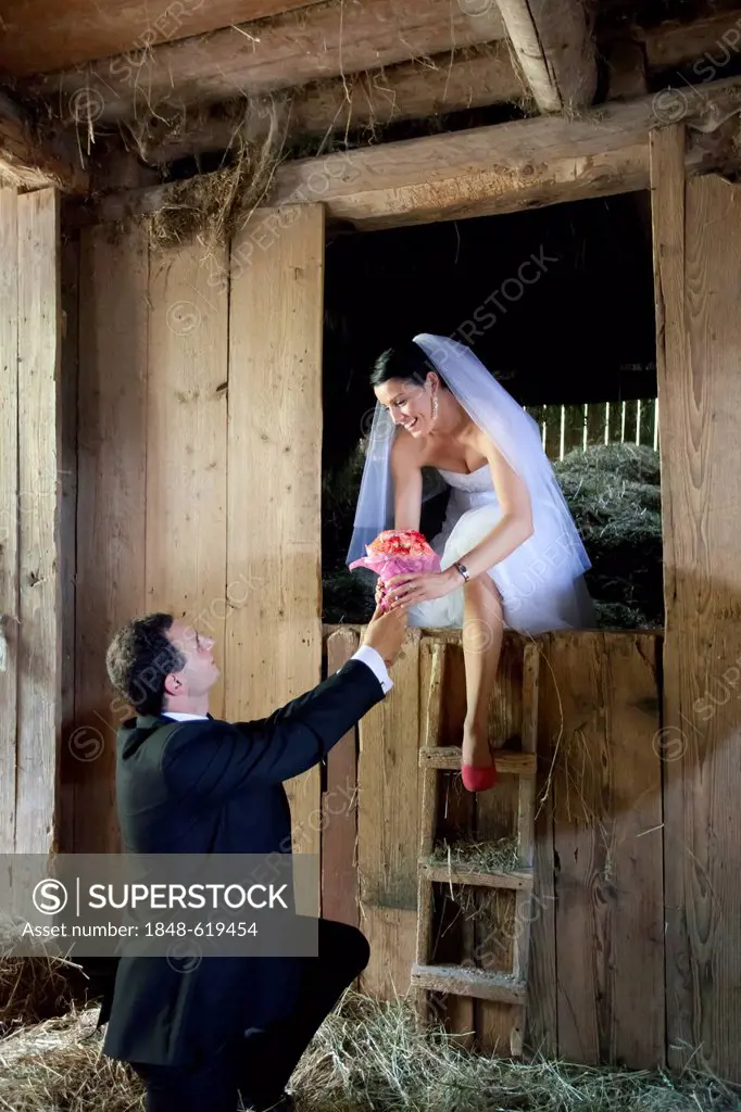 Bride and groom, bridal couple, bride looking out of a barn, hay shed, groom presenting flowers