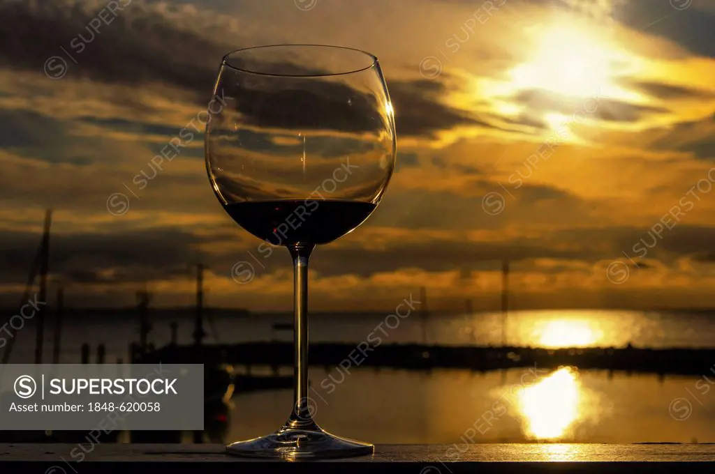 Glass of red wine on the rail of a balcony at sunset, overlooking the harbour, Timmendorf, Mecklenburg-Western Pomerania, Germany, Europe