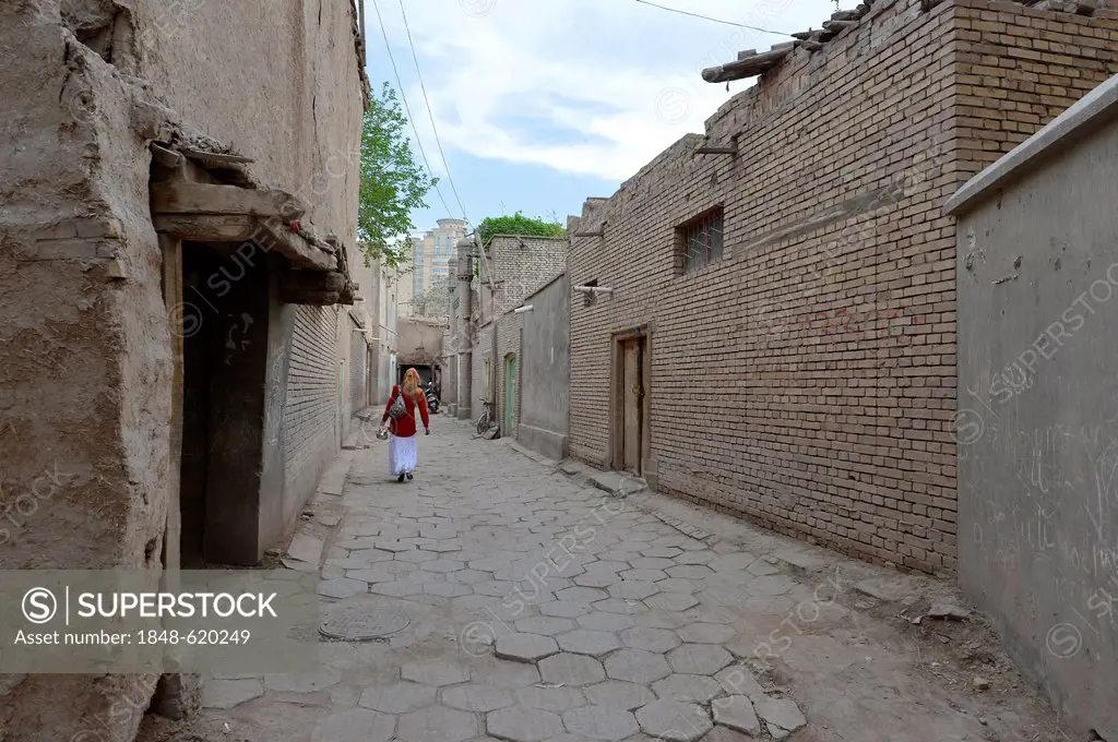Muslim woman walking though an alleyway in the old town of the Uyghur quarter, old adobe brick architecture, Silk Road, Kashgar, Xinjiang, China, Asia