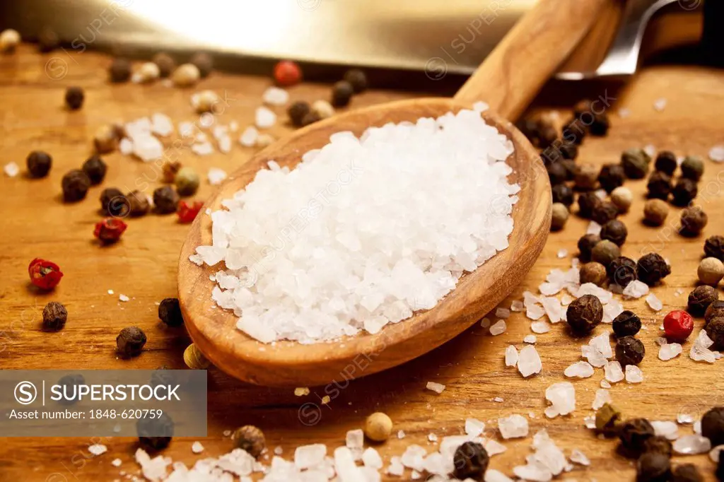 Wooden spoon with coarse sea salt, peppercorns next to it