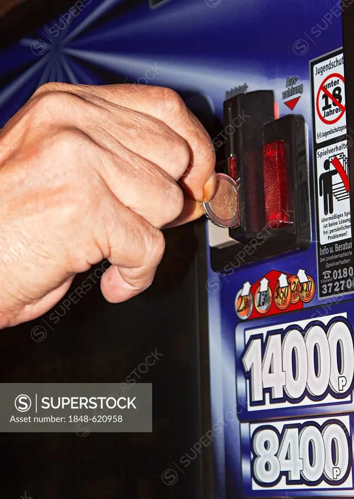 A man's hand is inserting a euro coin into a slot machine, warning sign, addiction to gambling