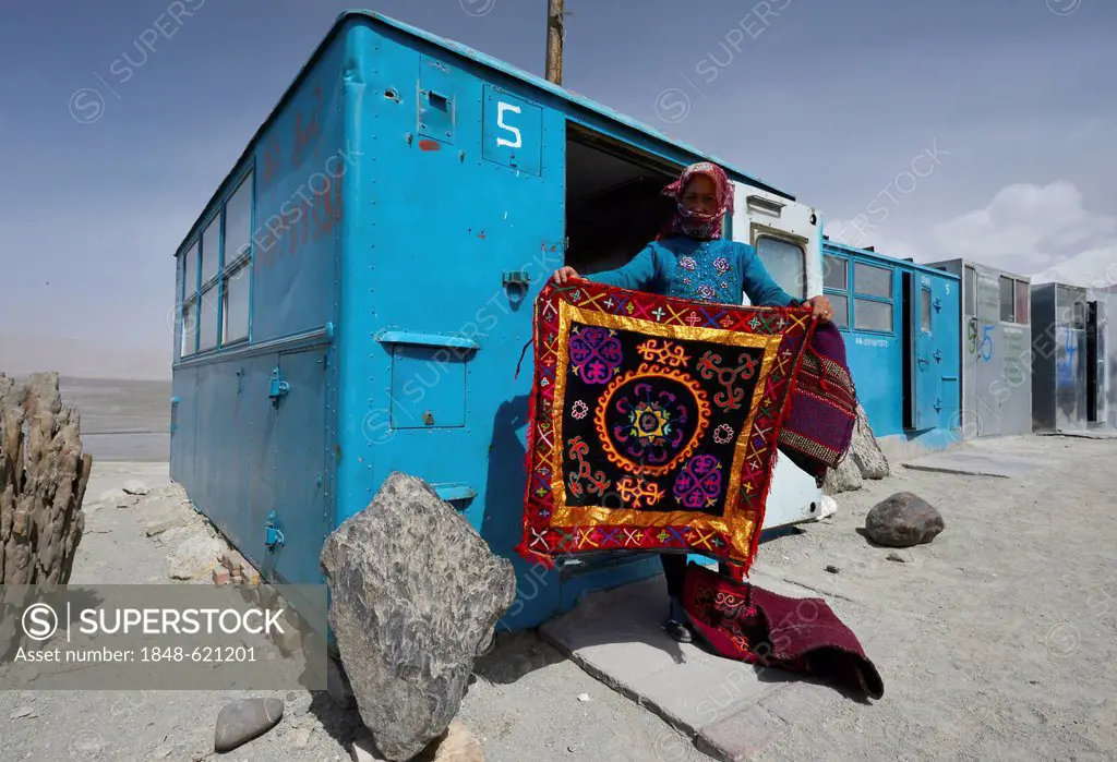 Kazakh woman showing a hand-woven, embroidered wall carpet, simple blue containers, house boxes, storage containers, shops of the Kazakhs in the Kongu...