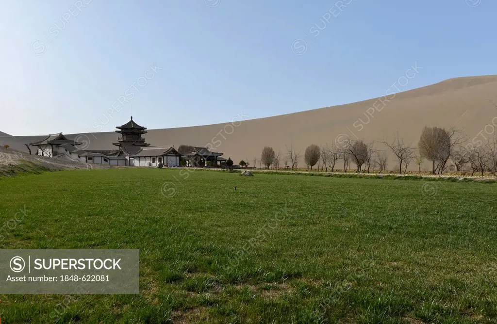 View from the sand dunes of the Gobi Desert to the Crescent Lake with a Chinese pagoda and a small green park near Dunhuang, Silk Road, Gansu, China, ...