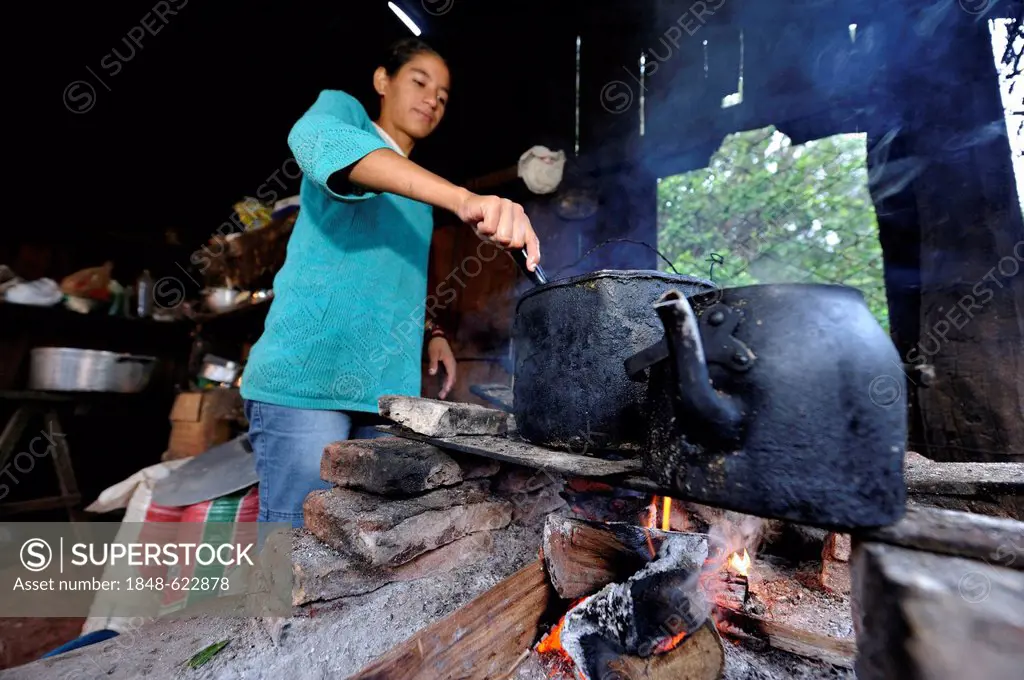 Young woman cooking over an open fire in the simple kitchen of farm workers, Comunidad Arroyito, Departamento Concepcion, Paraguay, South America