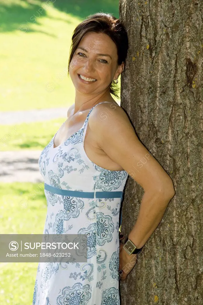 Smiling young woman leaning against a tree