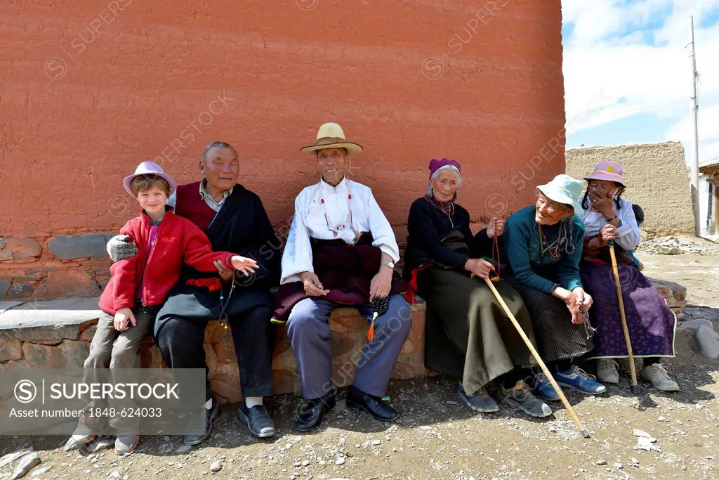 Tibetan Buddhism, Tibetan pilgrims, group of Tibetan seniors sitting together with a western child at the monastery walls, Labrang Monastery, Xiahe, G...