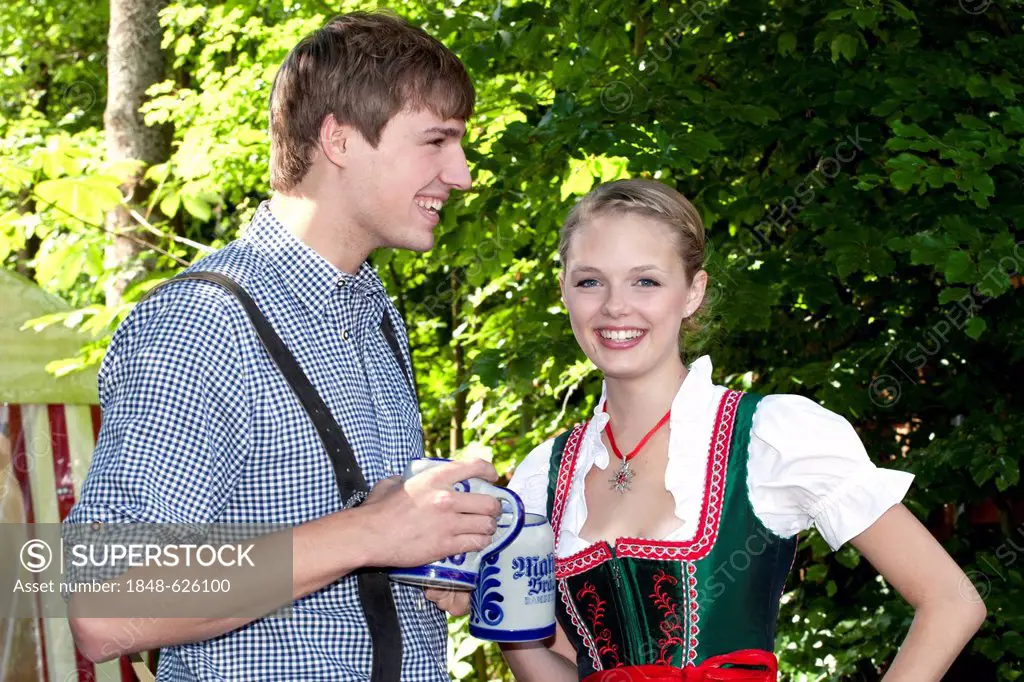 Young couple in dirndl and lederhosen standing in the beer garden, at Pettstatt, Upper Franconia, Bavaria, Germany, Europe