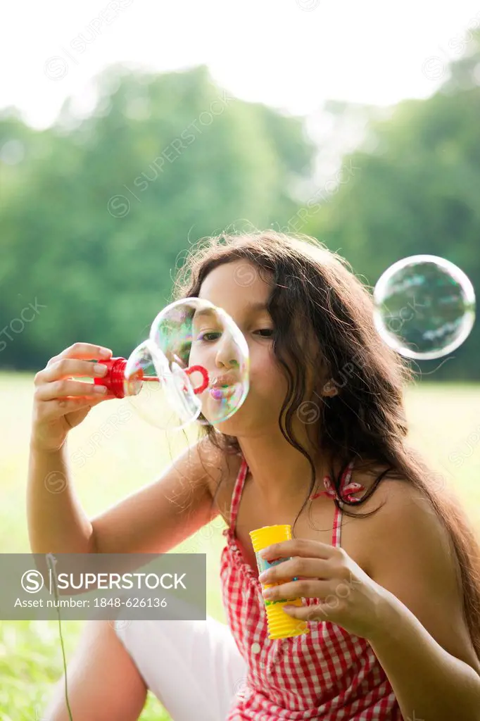Girl sitting on a meadow, blowing soap bubbles