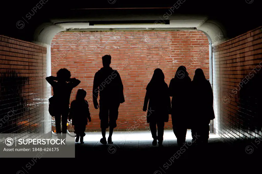 Young family with a child and a group of three women with headscarves, silhouetted in a pedestrian tunnel, Cologne, North Rhine-Westphalia, Germany, E...