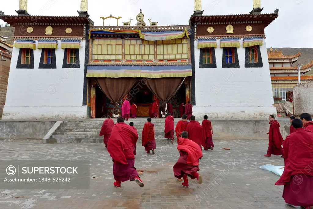 Tibetan Buddhism, Tibetan monks in red monk's robes running to the Puja ceremony in the monastery building, building in traditional architectural styl...