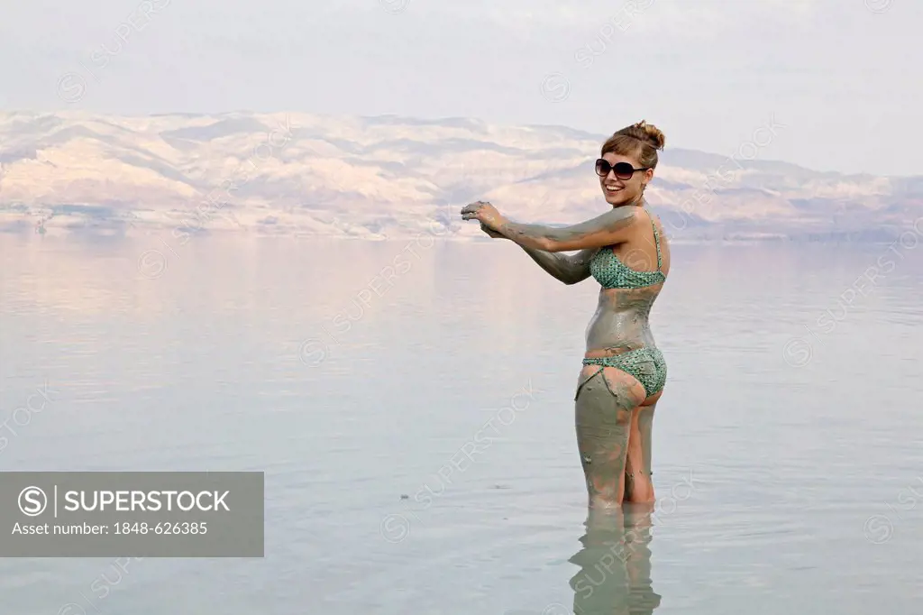 Young woman rubbing skin-soothing mud on herself, Dead Sea, West Bank, Israel, Middle East