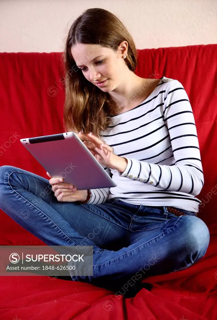 Girl sitting on a sofa holding an iPad, tablet computer with wireless internet access