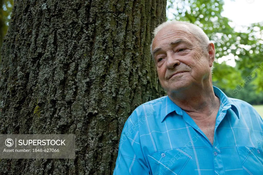 Elderly man standing next to a tree