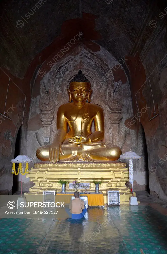 Burmese man sitting, praying in front of a golden Buddha statue, Old Bagan, Myanmar or Burma, Asia