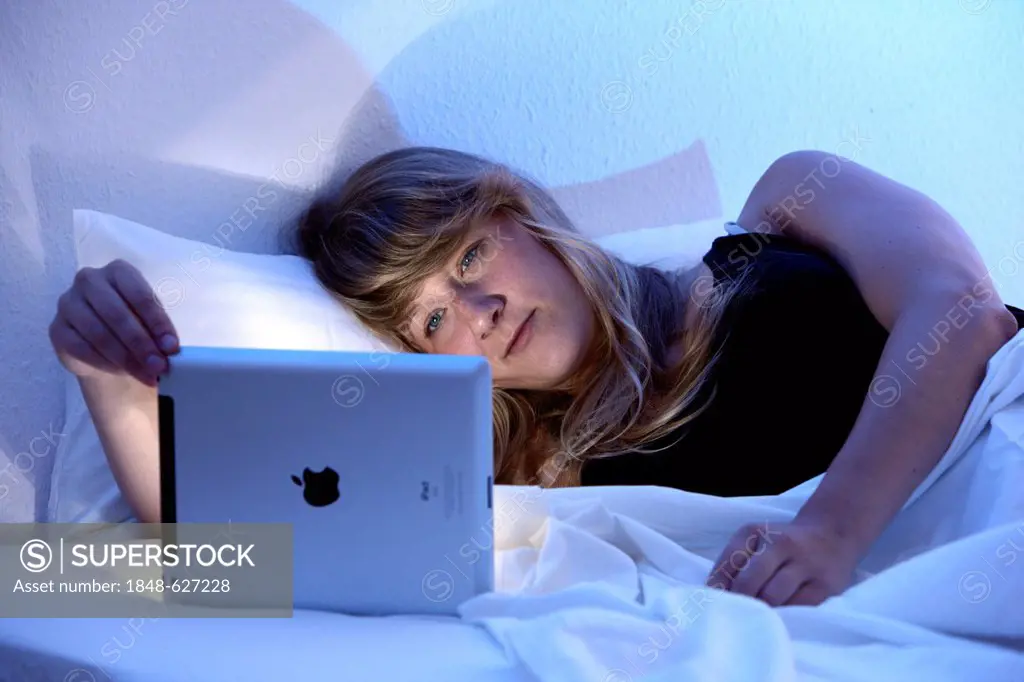 Young woman surfing in bed with an iPad, tablet computer, wireless internet access