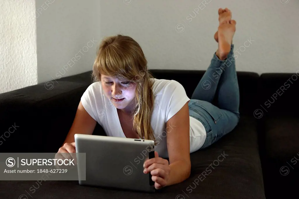 Young woman lying on a sofa surfing the internet, iPad, tablet computer with wireless internet access