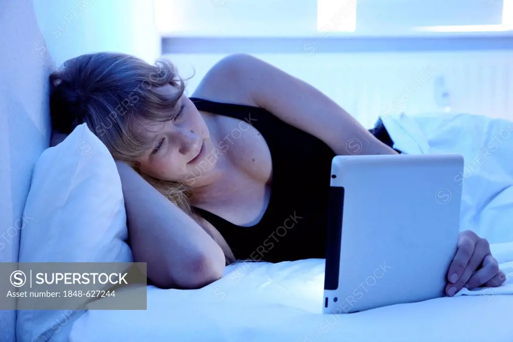 Young woman in bed surfing with an iPad, tablet computer in the internet via wireless connection