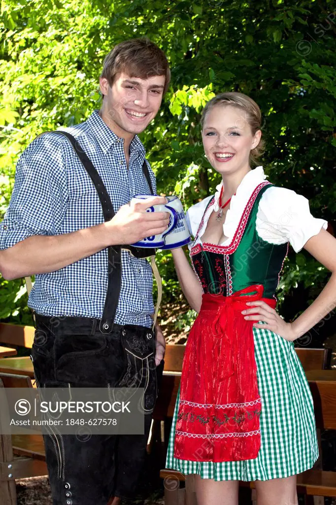 Young couple in dirndl and lederhosen standing in the beer garden, at Pettstatt, Upper Franconia, Bavaria, Germany, Europe