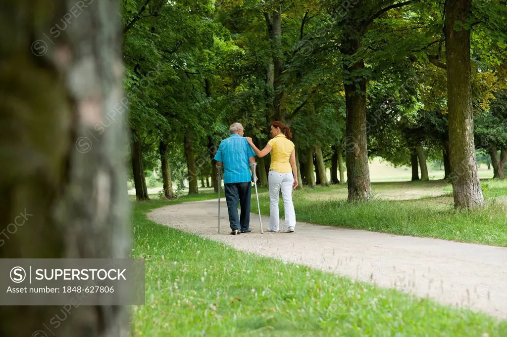 Woman and an elderly man on crutches strolling in the park