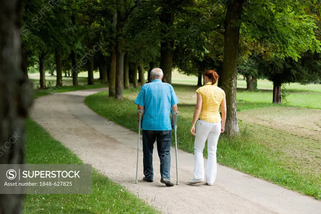 Woman and an elderly man on crutches strolling in the park