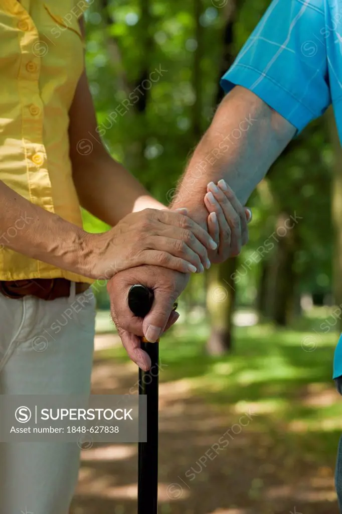 Woman putting her hand on the hand of an elderly man holding a walking stick