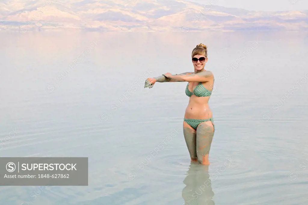 Young woman rubbing skin-soothing mud on herself, Dead Sea, West Bank, Israel, Middle East