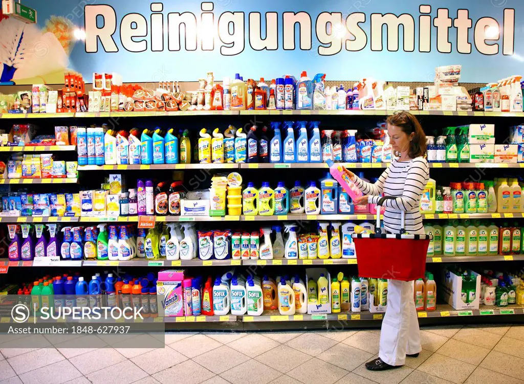 Woman looking at cleaning products in a corridor with household goods while shopping in a self-service grocery department, supermarket, Germany, Europ...