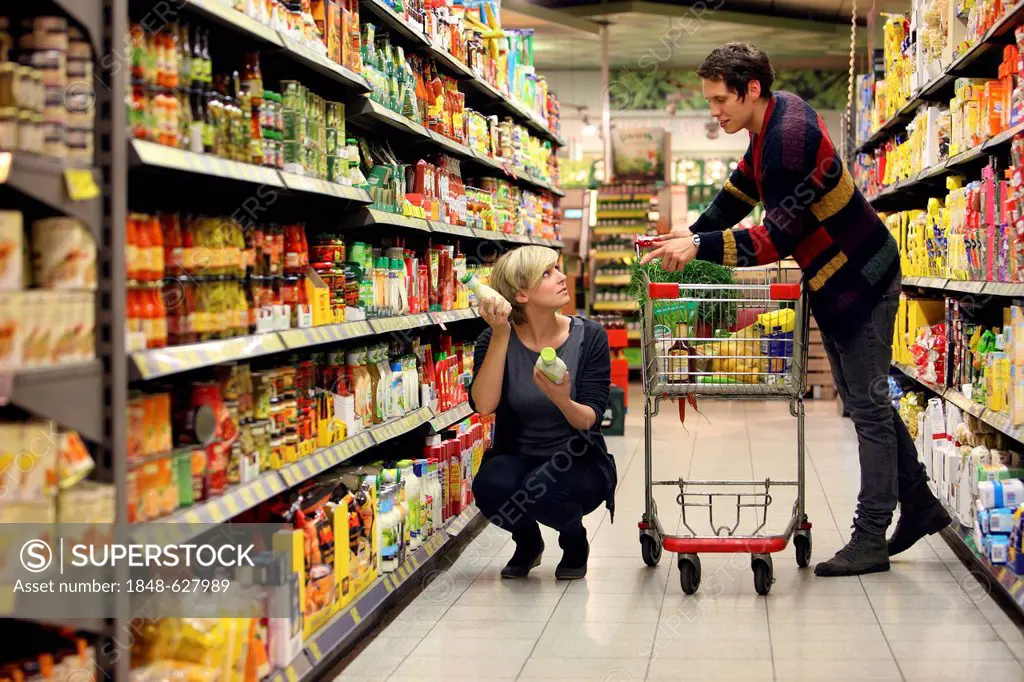 Young couple grocery shopping at the supermarket, shelves with various products, food hall, supermarket, Germany, Europe