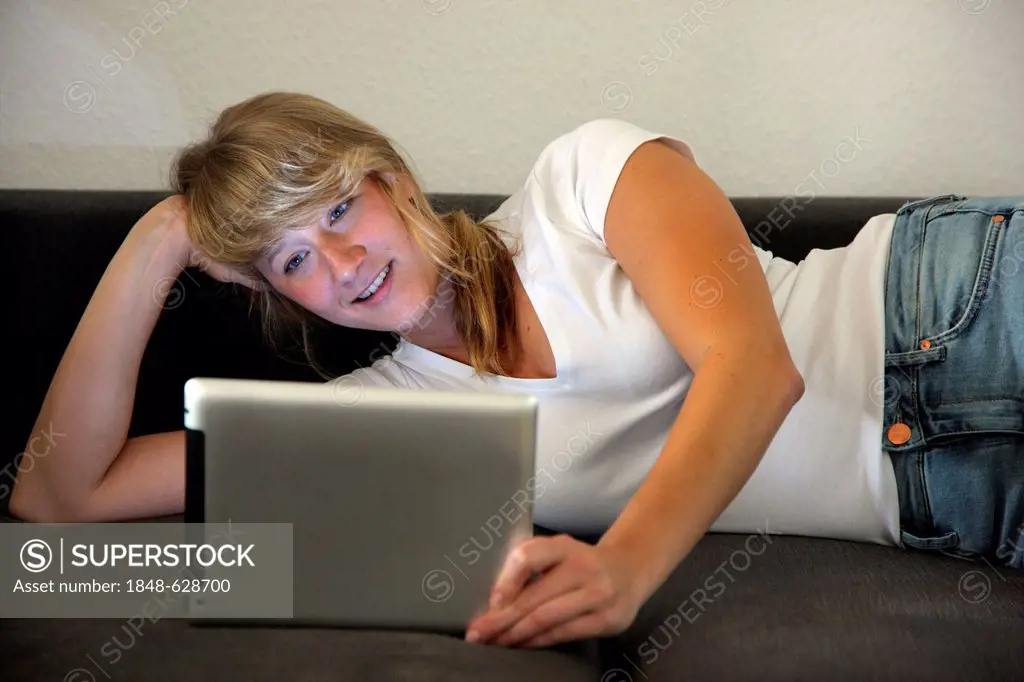 Young woman lying on a sofa surfing the internet, iPad, tablet computer with wireless internet access