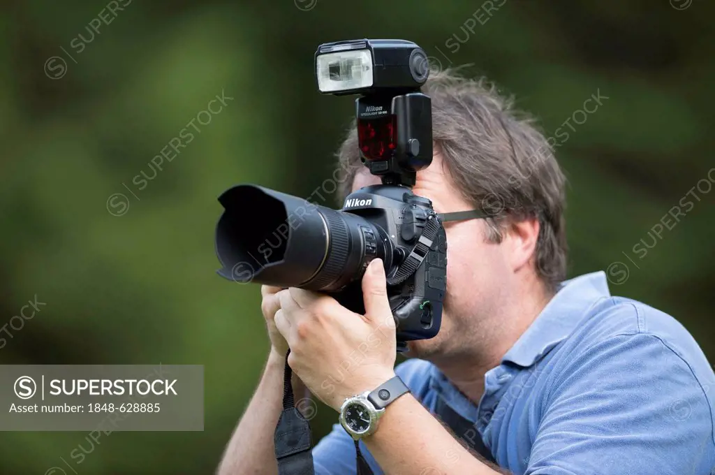 Photographer, mid 40's, taking pictures, looking through the viewfinder of a Nikon D4 digital SLR camera with a shoe-mounted flashgun