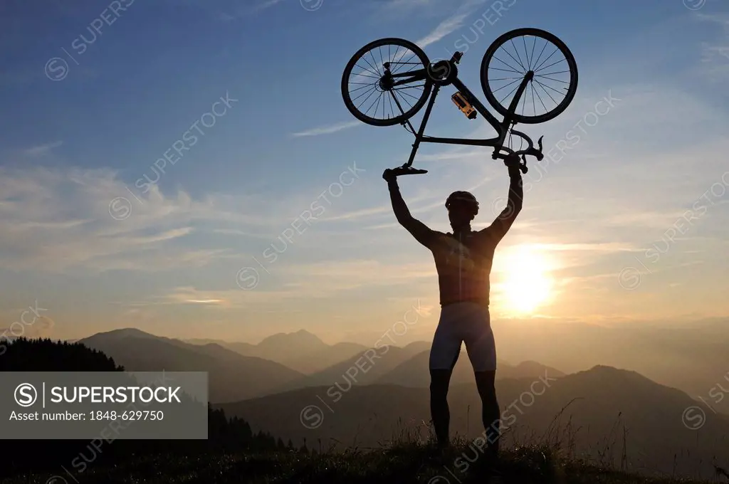 Man holding a racing bike above his head into the air, Kraftalm alp, Mt Hohe Salve, Kitzbuehel Alps, Tyrol, Austria, Europe