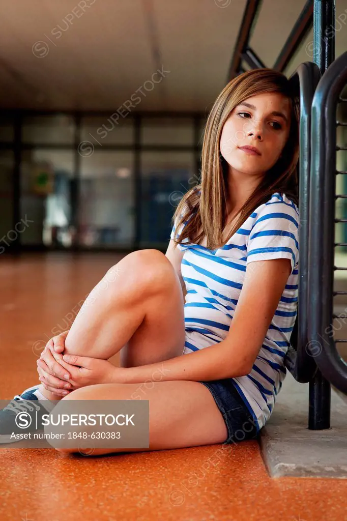 Schoolgirl sitting alone in the school building, leaning against a railing