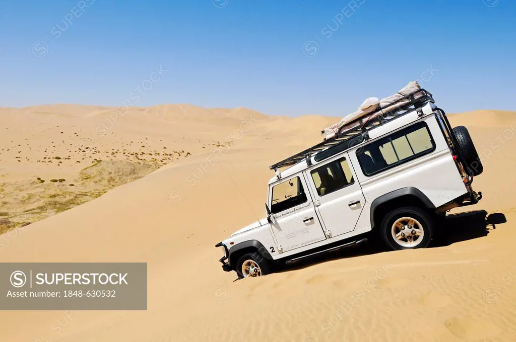 Landrover Defender off-road vehicle driving down a huge dune, Namib Naukluft National Park, part of the Namibian Skeleton Coast National Park, Skeleto...