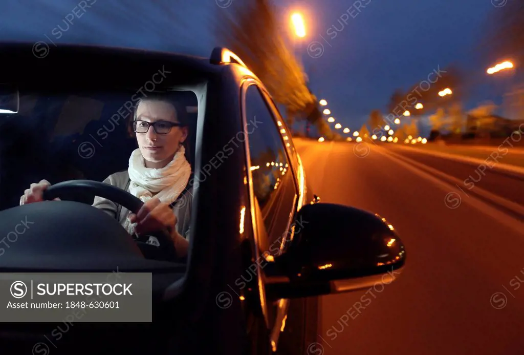 Young woman driving her car at night on a lit street
