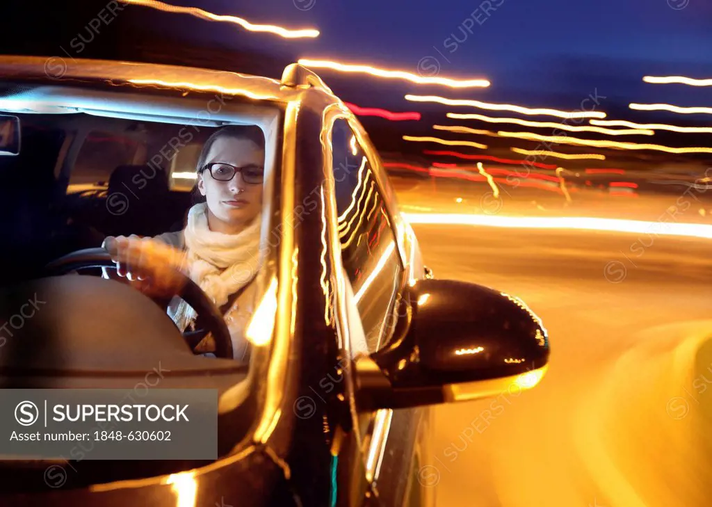 Young woman driving her car at night on a lit street