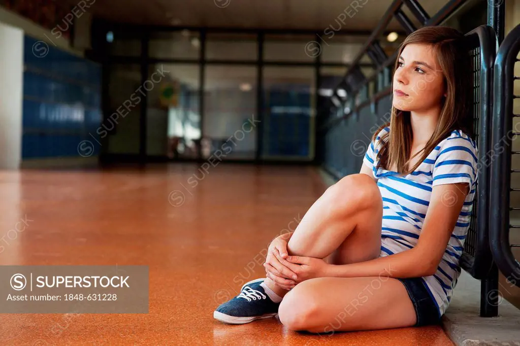 Schoolgirl sitting alone in the school building, leaning against a railing