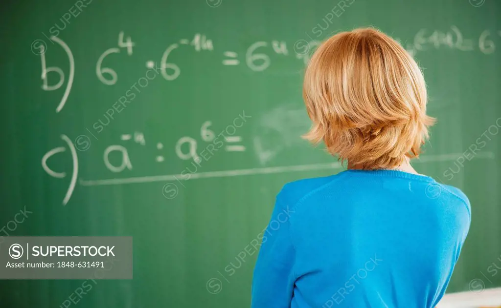 Schoolboy standing in front of a blackboard in a classroom, looking thoughtful