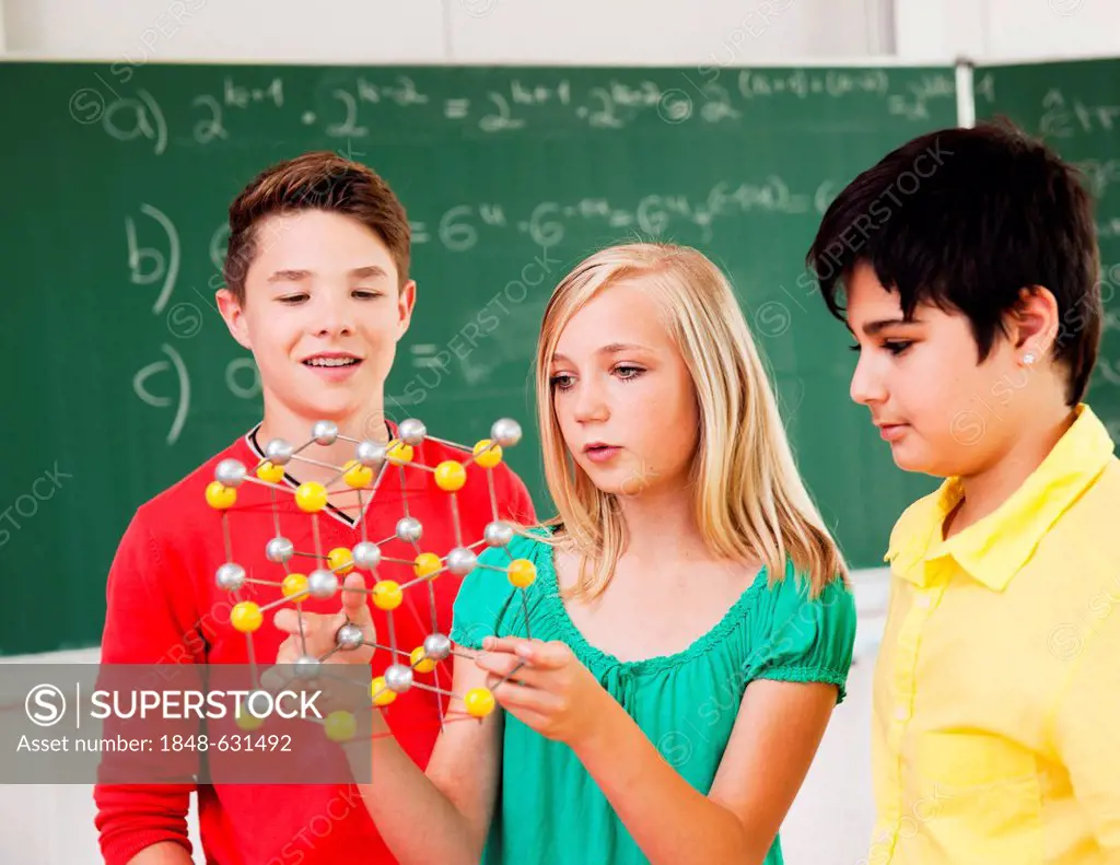 3 teenagers with a model of an atom in a classroom