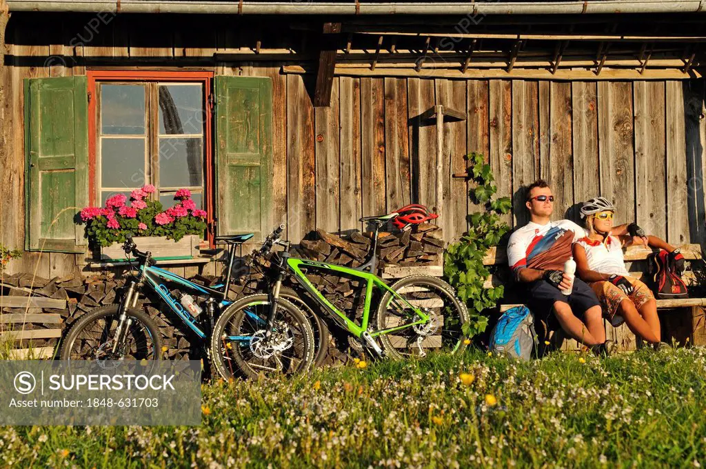 Mountain bikers resting in front of an old farmhouse on Kraftalm alp, Mt Hohe Salve, Kitzbuehel Alps, Tyrol, Austria, Europe