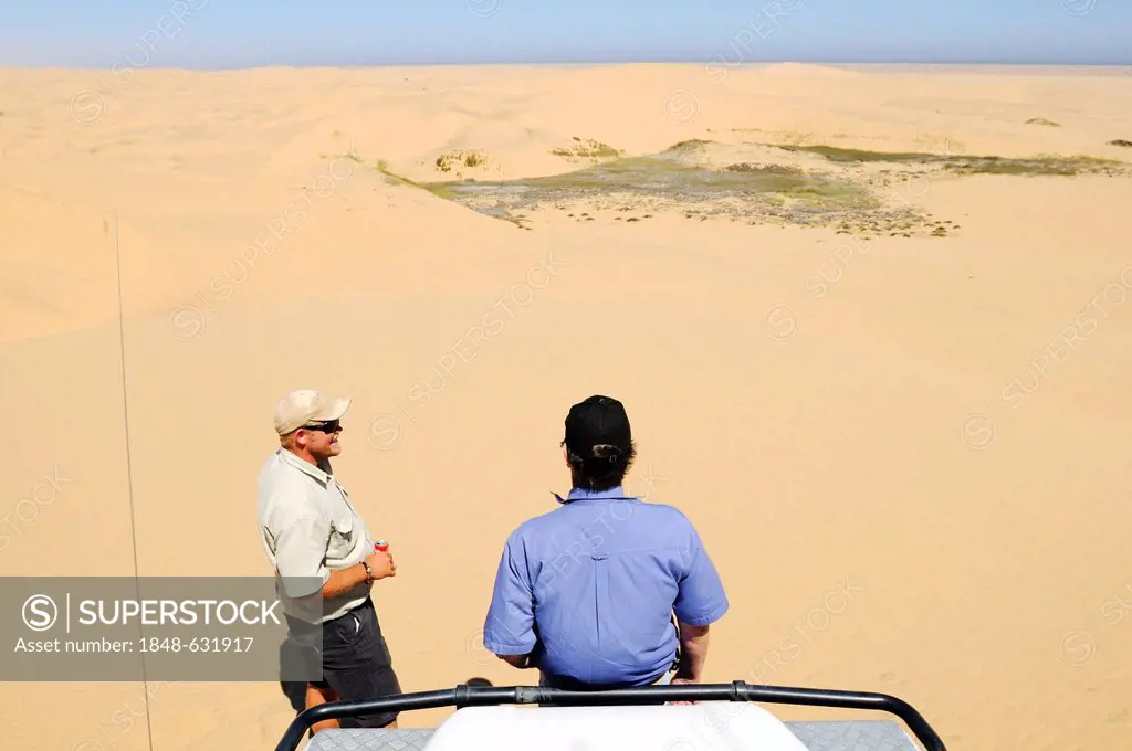 Two men with a Landrover Defender off-road vehicle in the dunes of the Namib Naukluft National Park, part of the Namibian Skeleton Coast National Park...